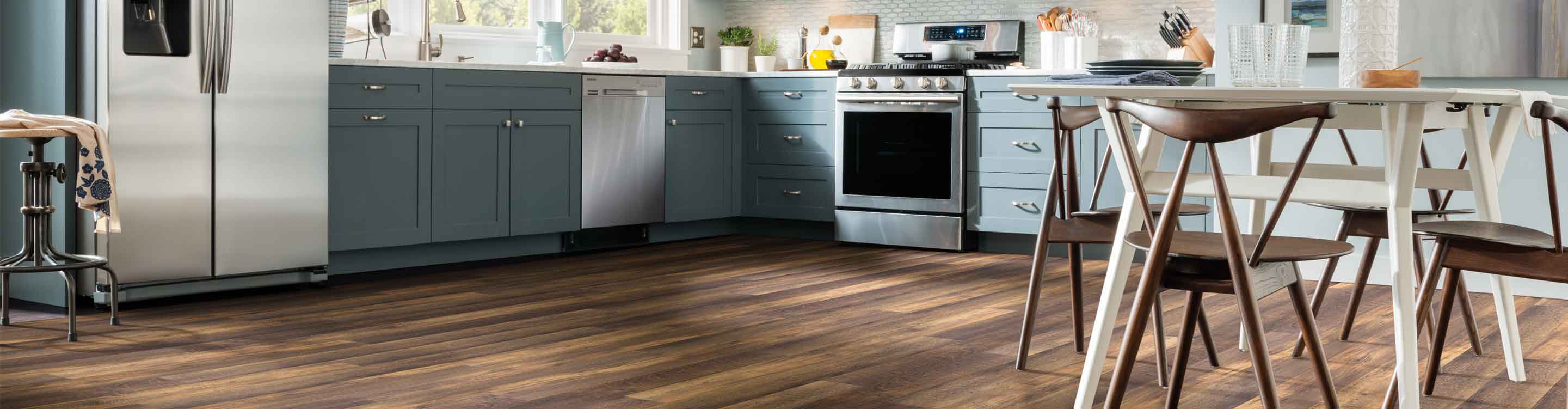 dark wood look vinyl flooring in modern kitchen with blue cabinets, white kitchen table and wooden kitchen chairs